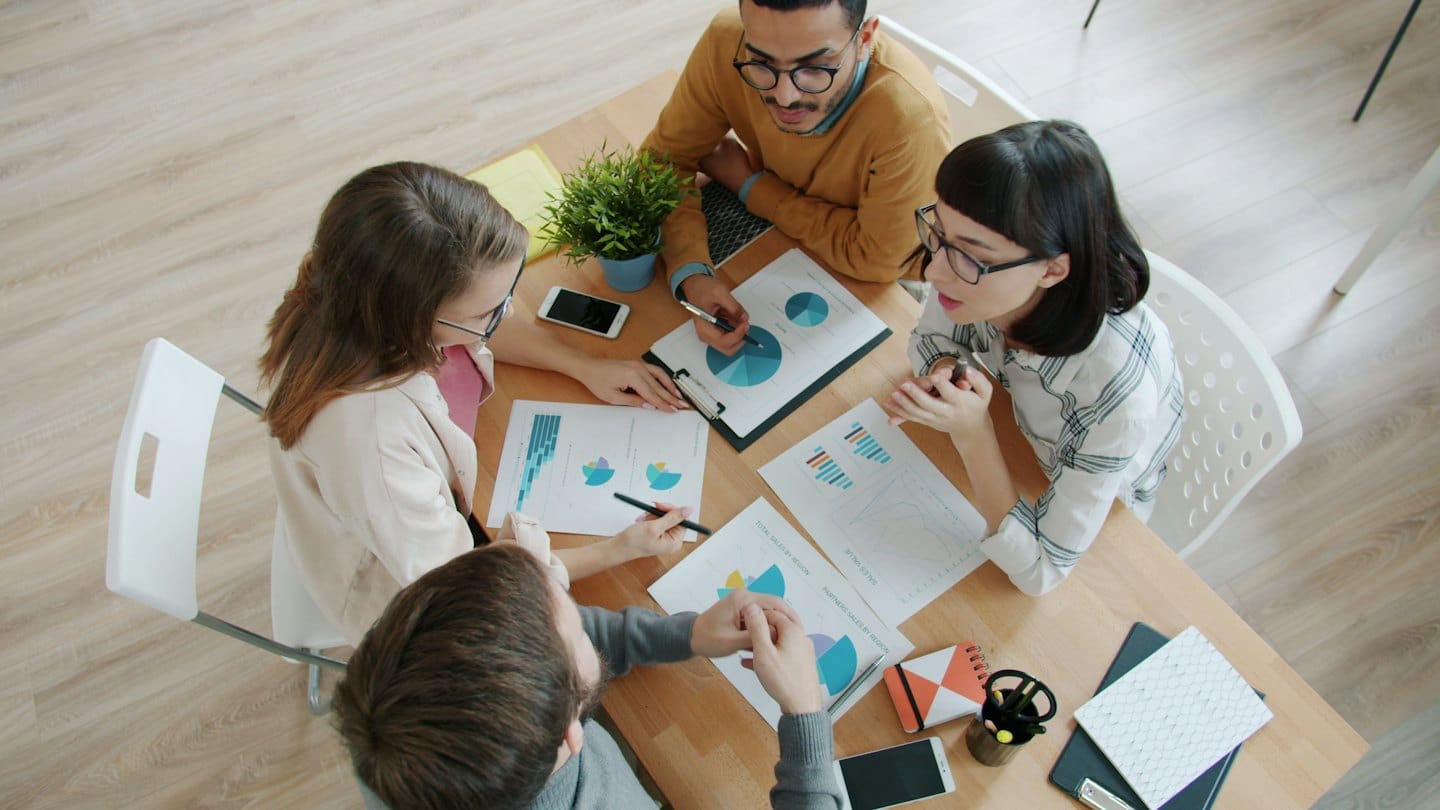 Diverse professionals discuss charts and graphs at a meeting table.